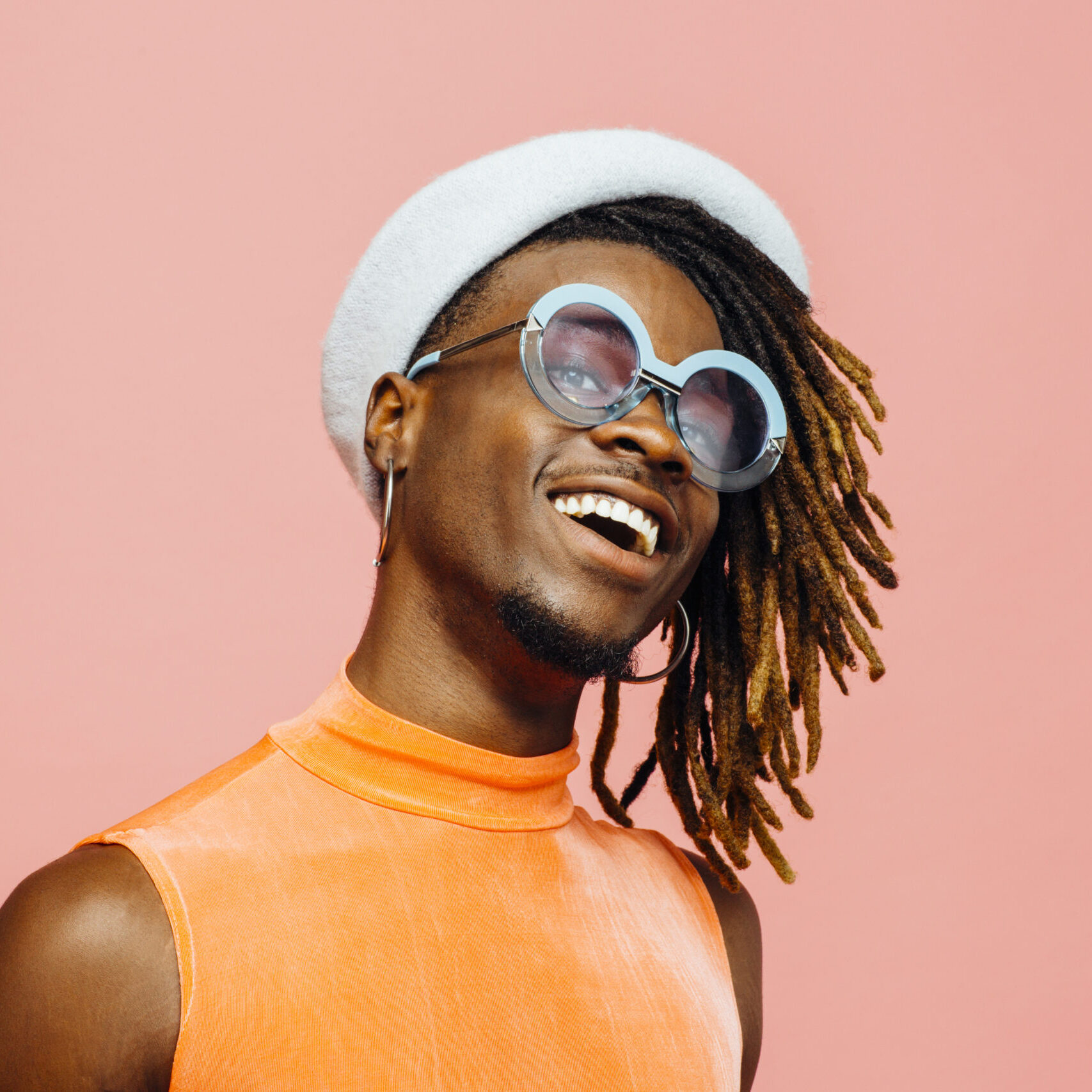 Portrait of a happy young man with sunglasses and cap laughing, isolated on pink